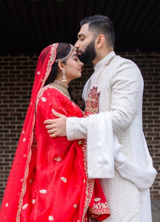 Bride in a red lehenga and groom in an ivory sherwani embracing at their Indian wedding at Wyndham Garden York