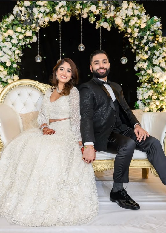 Couple seated on a sweetheart stage beneath a floral arch at their reception at Wyndham Garden York